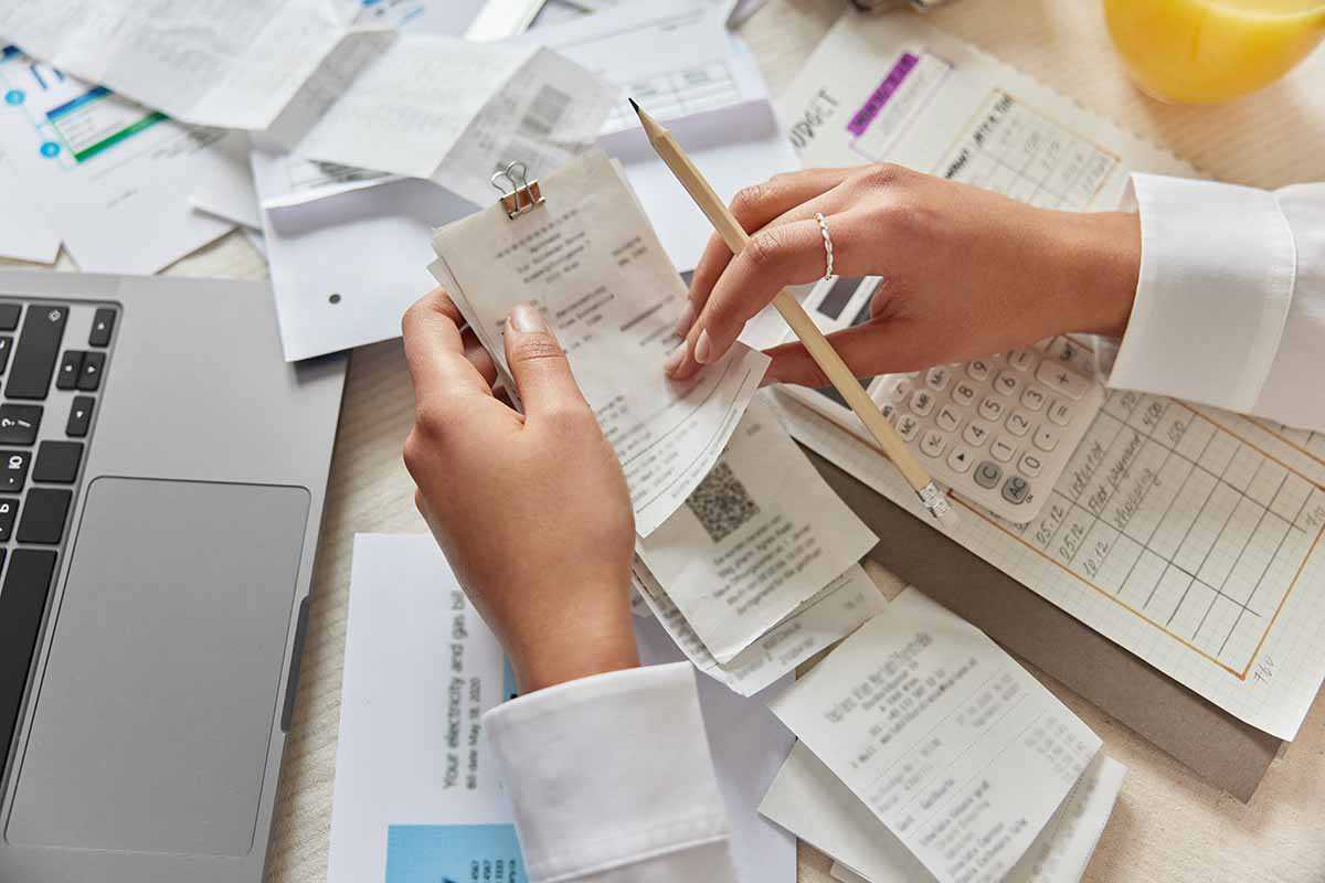 A businesswoman's hands holding receipts and a pencil with a calculator and laptop next to her