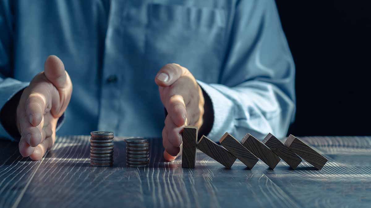 A businessman with coins and wooden dominos on his desk. His hands protect the coins from the wooden dominos hitting them