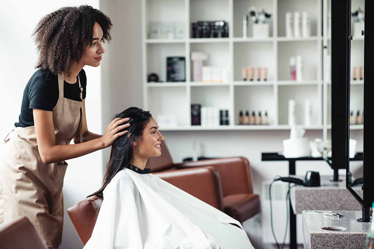 A young lady looking for a new style sitting in a salon chair while a young salon lady is talking to her to get ideas for a new style